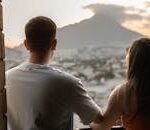A young couple shares a romantic moment, overlooking Monterrey's cityscape and mountains at sunset.