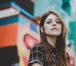 Portrait of a fashionable woman with glasses posing confidently outdoors in front of a vibrant mural.