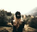 A woman in black cap and sweater enjoys a mountain view, embracing outdoor adventure.
